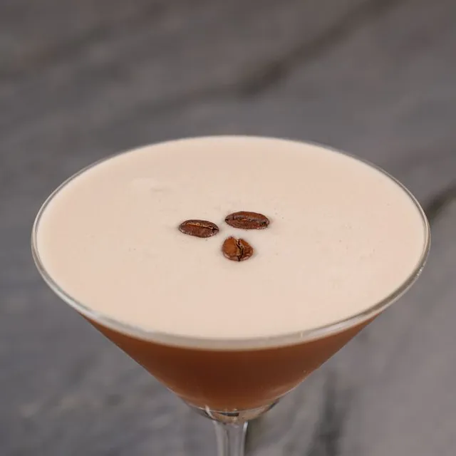 An espresso martini with a creamy top and three coffee beans.