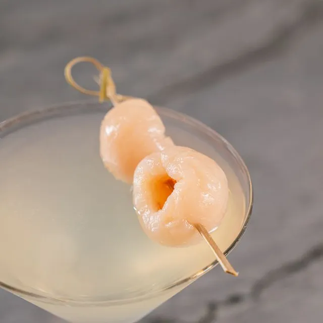 A clear martini garnished with two lychees on a pick.