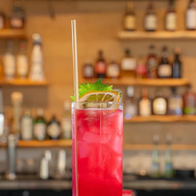 A bright red highball with a dried lemon wheel and a shiso leaf.
