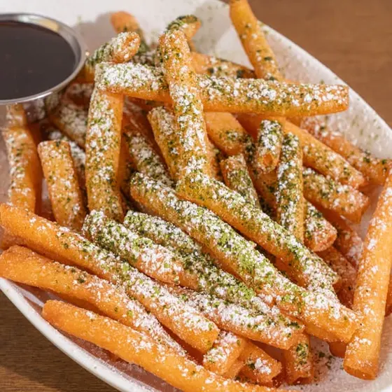 Matcha funnel sticks dusted with matcha sugar, with a dipping sauce.