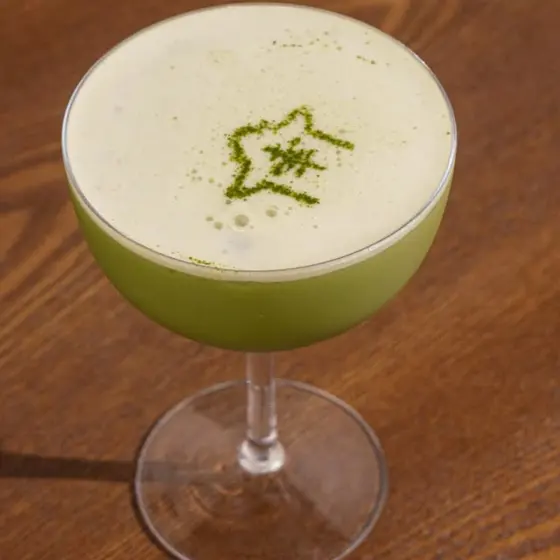 A green matcha cocktail with a frothy top and a matcha star.