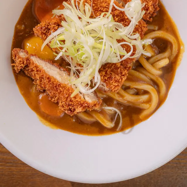 Chicken katsu curry with udon, topped with thinly sliced green onions.
