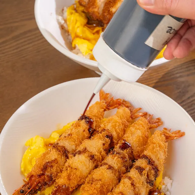 Sauce poured over a shrimp katsu bowl: four crispy fried shrimp on egg and rice.